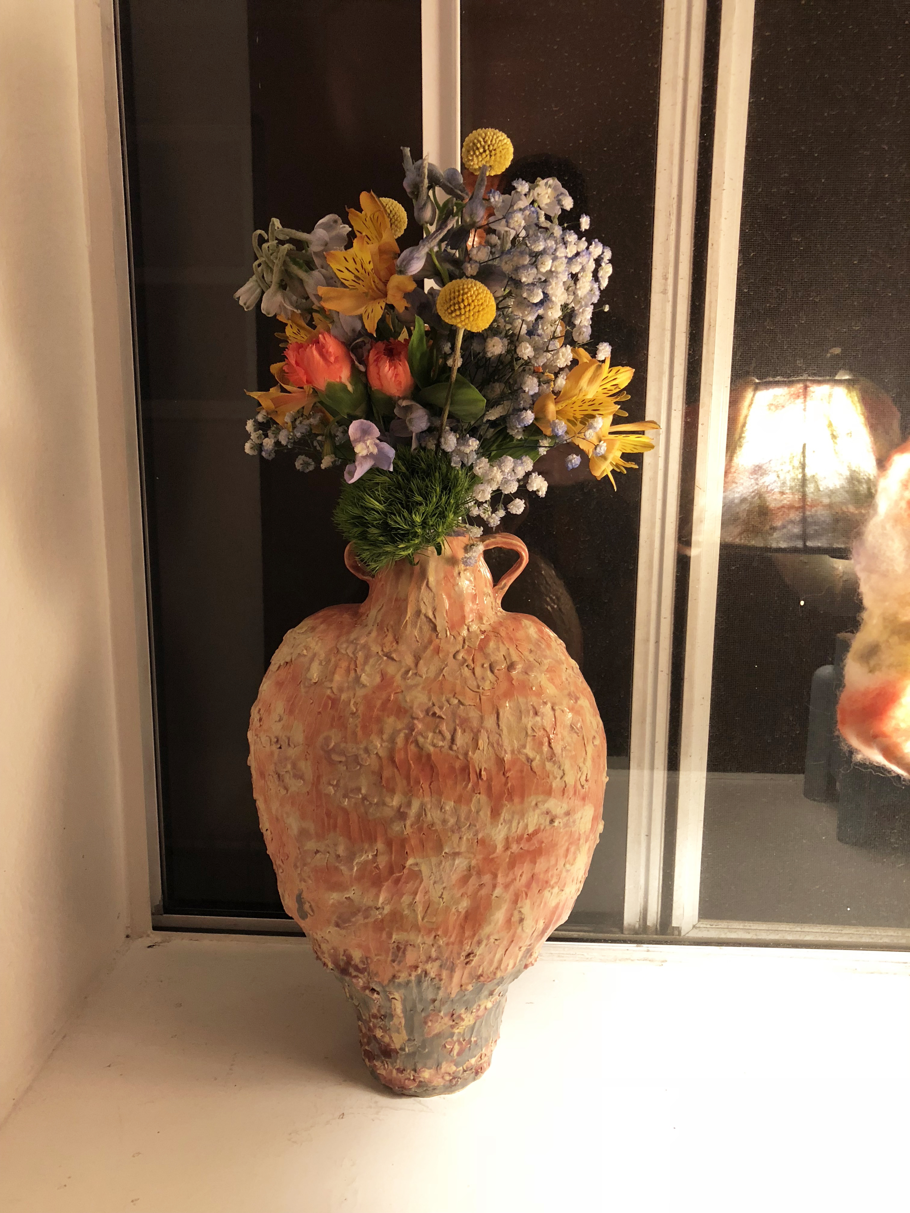 An orange ceramic vase with flowers on a windowsill